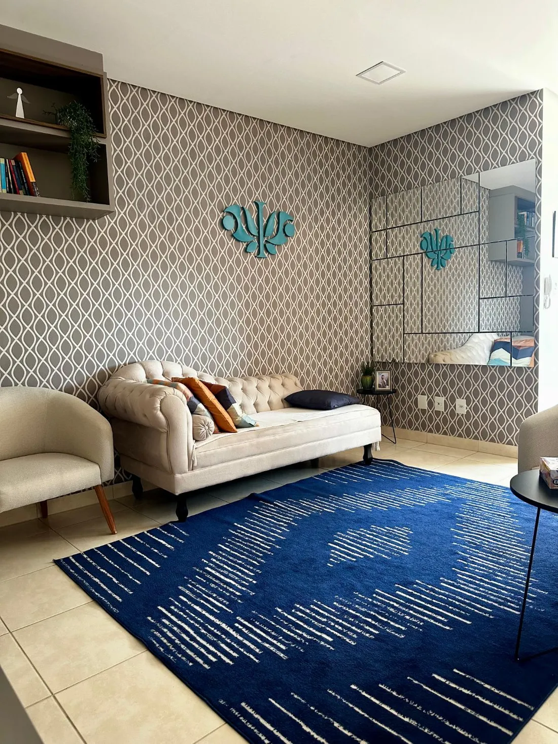 Sala de atendimento com divã claro, poltrona, tapete azul e o símbolo da psicologia na parede